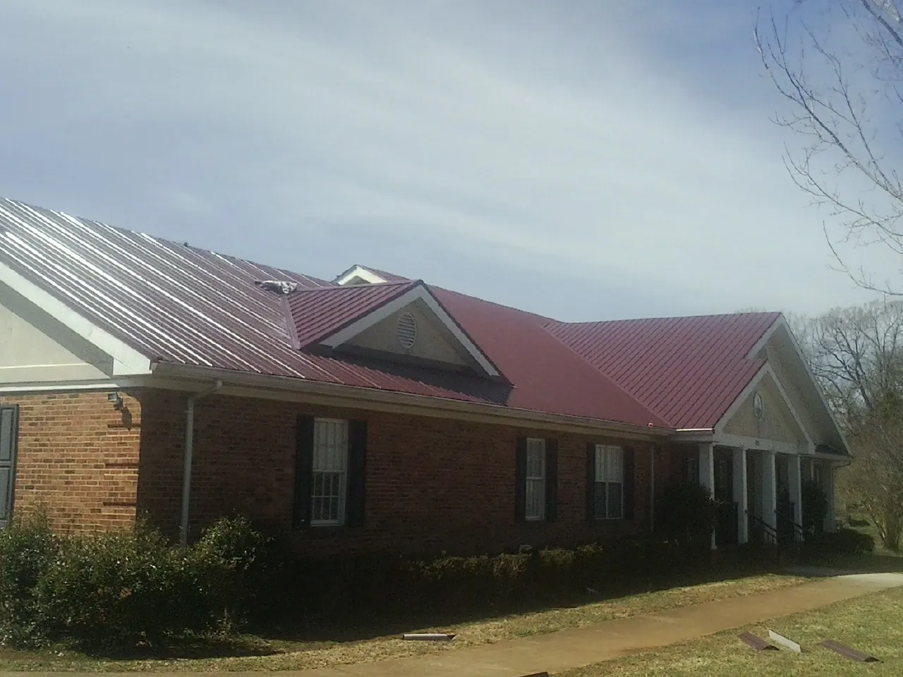 Red metal roof with gabled entries on a long brick building, from a Hail Damage Roof Repair job in Granbury