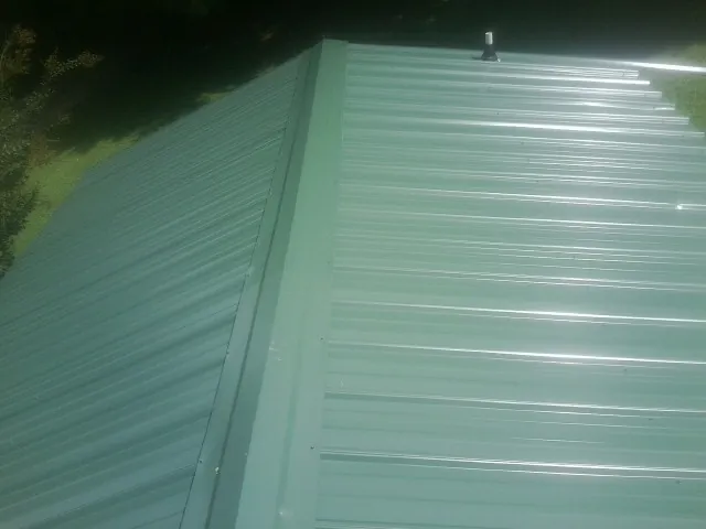 New green metal panels meeting at the ridge of a roof — Flat Roof Repair work by our crew in Granbury