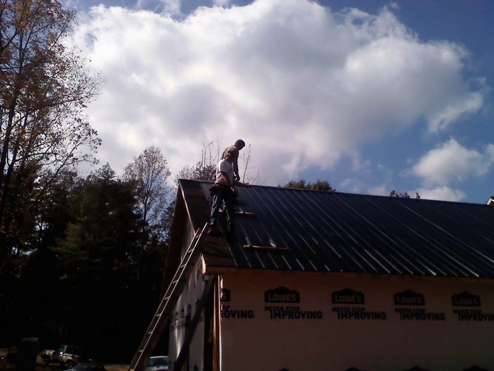Roofer fastening dark metal panels high against a cloudy sky, from a Roof Inspection job in Granbury