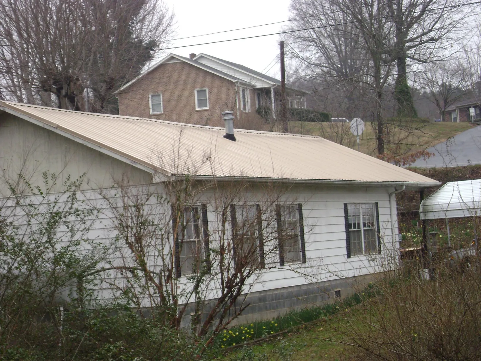 Tan metal roof on a white sided house set into a hillside — Commercial Roofing by Roofing Brothers in Granbury